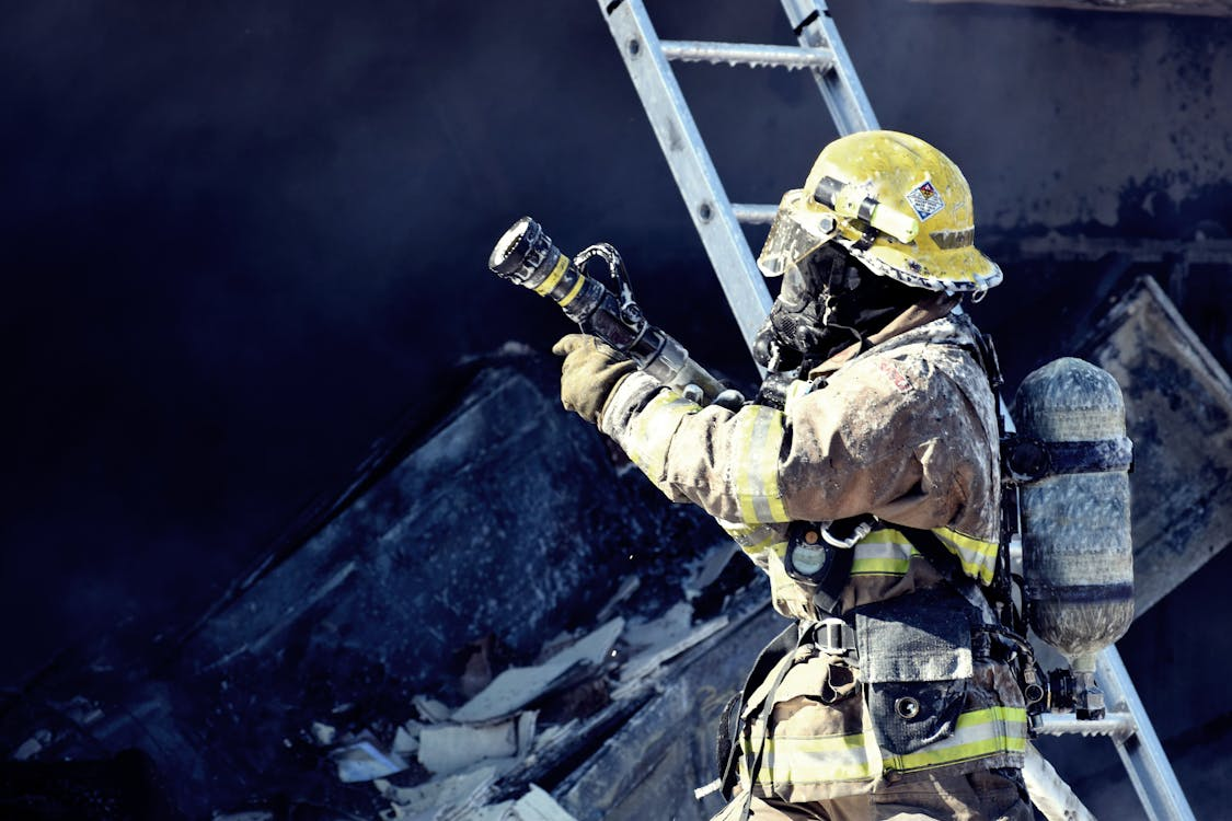 A firefighter holding a water hose in hand wearing yellow and brown coveralls