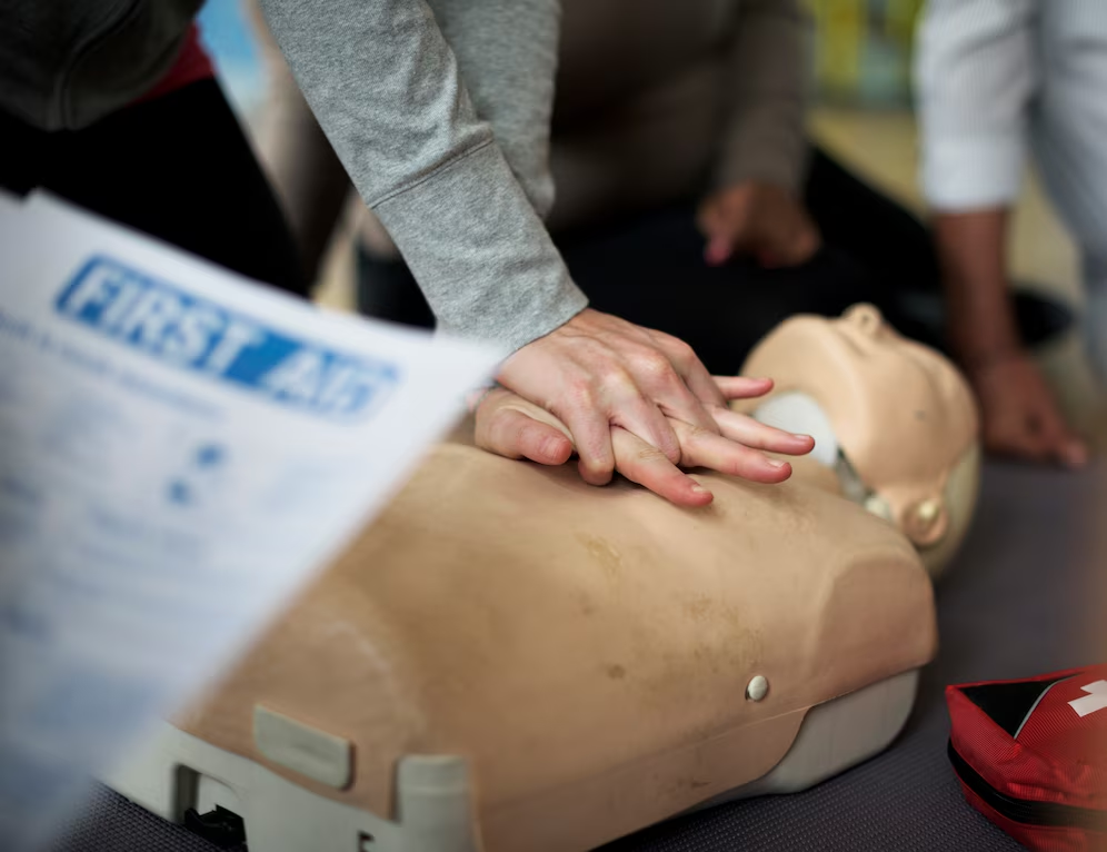 A person receiving first aid training, practicing CPR under trainer's monitoring